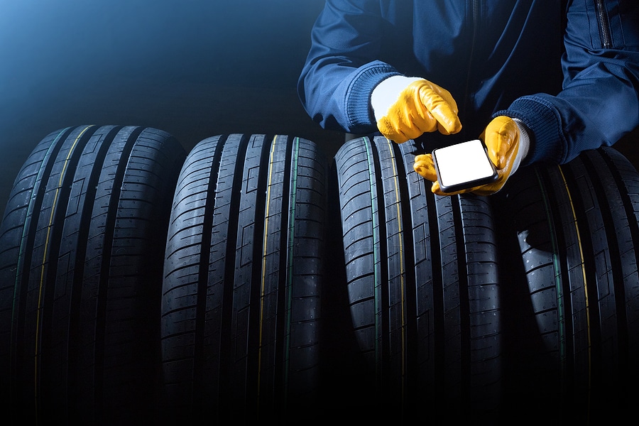 Image o a mechanic holding a smart phone over a row of car tires on Hollenshade's automotive services website